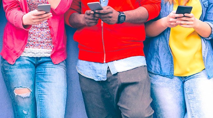 Grupo de jovens encostados em uma parede lendo no celular sobre o pix no blog bmg